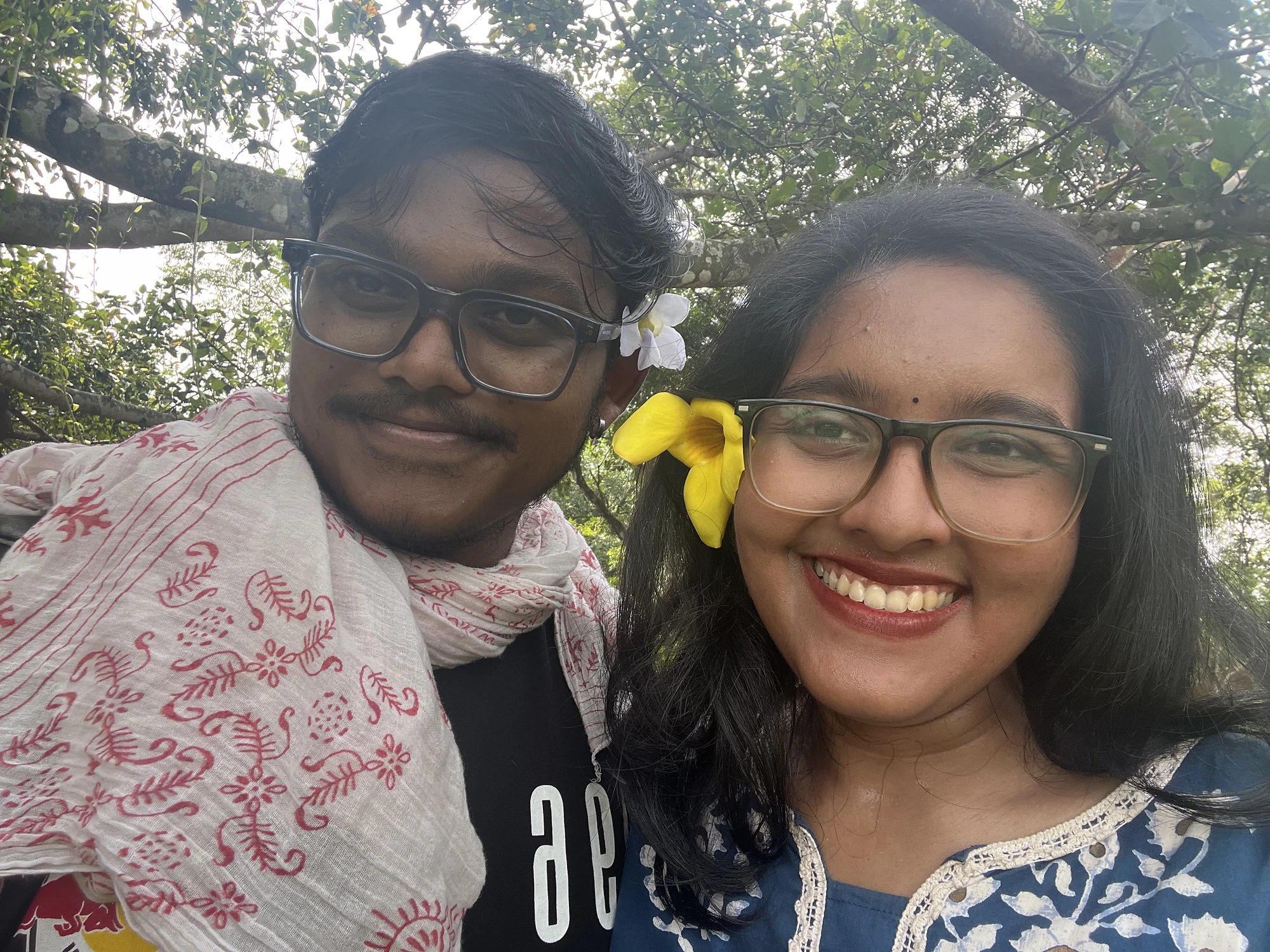 Smiling together beneath the trees with a yellow flower